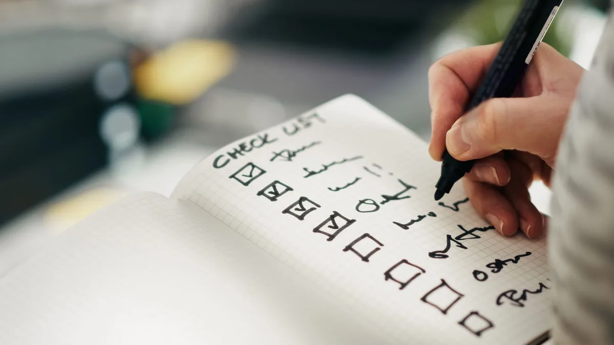 Dłoń odhaczająca punkty listy kontrolnej w notesie